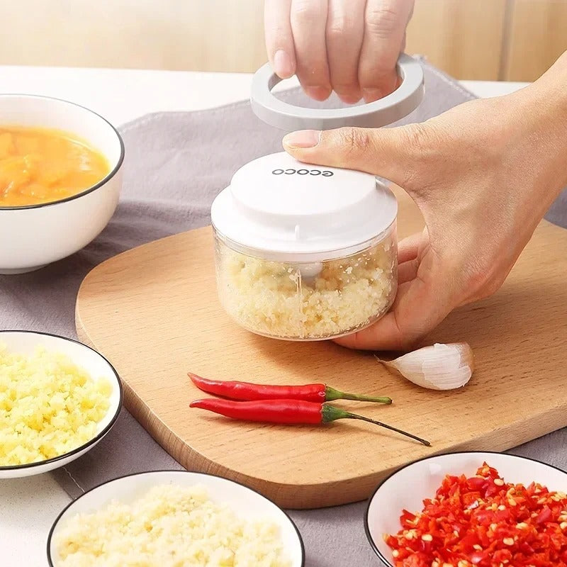 Compact, transparent food processor with a black lid and sharp stainless steel blades, designed for easy chopping and blending of ingredients.

