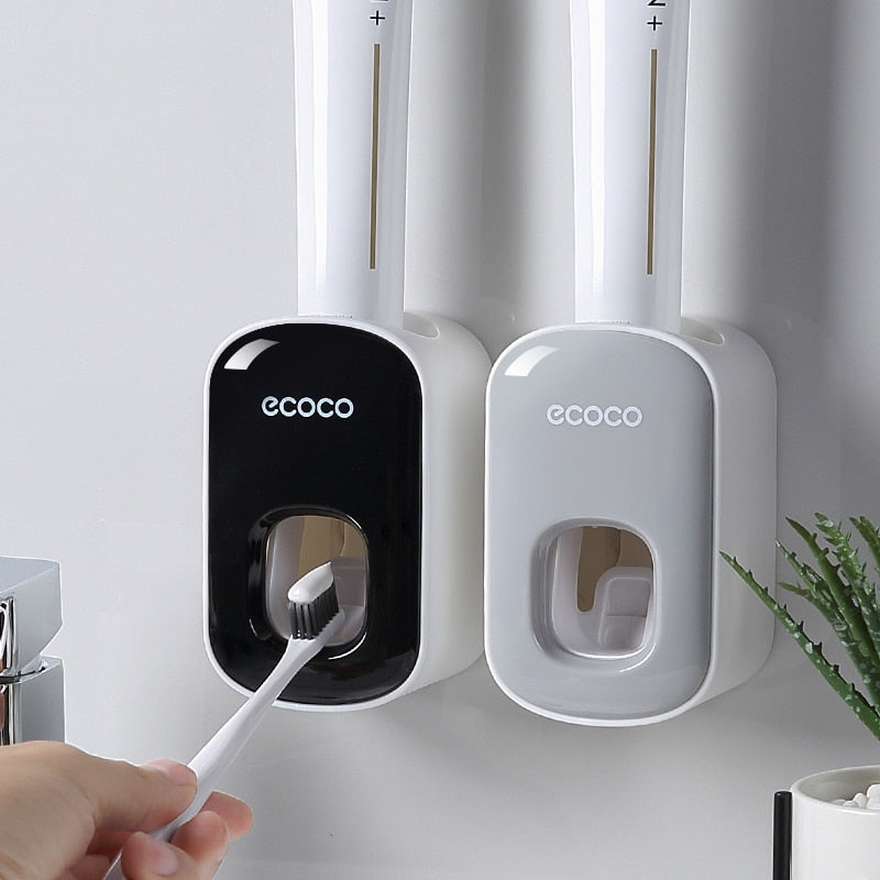 Simple gray Ecoco toothpaste dispenser mounted on a wall near a bathroom faucet for convenient use.